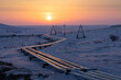 Winter arctic industrial landscape. View of a pipeline and electrical towers in the snowy tundra of the Arctic. The setting sun is above the horizon. Sunset. Industry and ecology in the polar region.
