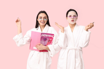 Poster - Young women in bathrobes with facial mask, under-eye patches, lip balms and magazine on pink background