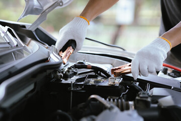 Close-up of auto mechanic charging car battery with electric rail jumper cables	