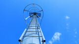 Fototapeta  - Staircase on spotlight pole. Ladder for maintenance of stadium light poles in bottom view on blue sky background with copy space with selective focus.
