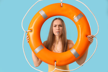 Wall Mural - Young female lifeguard with rescue ring whistling on blue background