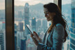 © Welle Photos - A young businesswoman is smiling while using her tablet in an office with large windows overlooking the city.
