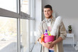 Young bearded man with bucket of cleaning supplies near window at home