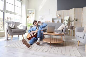 Poster - Young tattooed man in headphones playing guitar at home