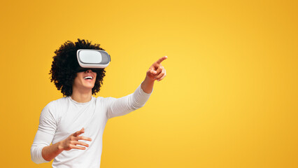 Wall Mural - African-american guy enjoying virtual reality glasses, pushing invisible button, orange background with free space