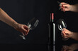 Bottle of red wine and hands with corkscrew and wine glasses.