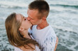 Face closeup. Female kissing and hugging male stand on beach ocean and enjoy sunny summer day on vacation. Woman kisses man on sand sea. Couple in love embraces on the seashore. Spend time together