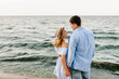Happy couple in love holding hands and looking at each other on the seashore. A man and a woman are standing on the sand near the ocean. Vows and promises on the seashore.