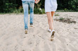 Legs down view. Bottom view of feet. Man and woman walking on sand sea. Back view. Couple in love holding hands on seashore. Female and male running on beach enjoying summer. Spending time together