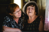 Fototapeta  - An older woman and her adult daughter sit together, their expressions conveying a lifetime of love, wisdom, and connection.
