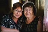 Fototapeta Sawanna - An elderly woman and her grown daughter share a tender moment in the portrait, reflecting the passage of time and the enduring bond between generations.