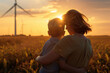 © kalafoto - A mother standing with her child on a mountaintop, watching wind turbines at a wind farm in the distance under the setting sun.