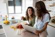 © Dorde - Two beautiful young women preparing meal together at home using laptop for delicious recipes.