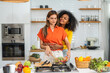 Diversity young happy love LGBT, LGBTQ caucasian and african family lesbian couple woman cook vegan food healthy eat with fresh vegetable salad in kitchen at home, pride, rainbow.Lgbt lesbian couple