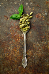 Wall Mural - Fragrant cardamom seeds in a metal spoon. Spices and condiments. Top view. On a dark background.