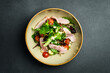 Fresh veal salad with spinach and arugula. On a black stone background. In a plate, close-up.