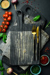 Creative kitchen banner. Cutting board, cutlery, spices and kitchen utensils on black stone background. Free space for text.