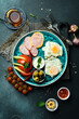 English breakfast. Fried eggs, salami, bacon and vegetables. Tea and sweets. On a dark slate background.