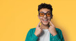 Dental dent care ad concept image - сurly haired funny young man wear metal braces, sunglasses glasses, show point white teeth smile. Isolated against yellow wall background. Positive optimistic.