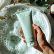 Hand holding a skincare tube over a bubbling bath, emphasizing the clean and fresh beauty product, mock up