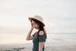 © David - A beautiful young Asian girl is holding her straw hat on the beach during sunset with bokeh background