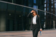 Sophisticated businesswoman walking confidently near glass buildings, looking slightly away