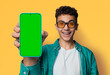 Shocked happy man wear sunglasses glasses, braces, open mouth, show cell phone, smartphone, mobile phone, green chroma key mockup mock screen, isolated yellow wall background. Online offer ad