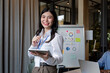 © Natee Meepian - Smiling business looking at camera and standing in an office at team meeting. businesswoman with colleagues in boardroom while holding digital tablet