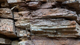Fototapeta Sport - A rocky cliff with a brown and red color. The rocks are piled up and the ground is covered with dirt