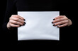Female hands with black manicure holding a blank white sheet of paper