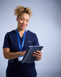 Studio Portrait Of Female Nurse Wearing Uniform With Digital Tablet Against Grey Background