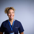 Studio Portrait Of Smiling Female Nurse Wearing Uniform With Security Lanyard On Grey Background