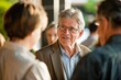 © Ilia Nesolenyi - A middleaged businessman wearing glasses engaging in conversation with a group of people at a networking event, showcasing interpersonal skills and relationship-building