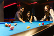 Young diversity group of people playing pool together with smile, enjoyment and fun. Young people spend time in billiards room at the nightclub. Men, women friends playing billiards. Nightlife concept