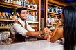 Caucasian professional bartender or mixologist making a cocktail for women at a bar. An attractive barman served a glass of wine with a smile to a woman. Bartender service at the night club restaurant
