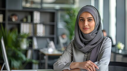 professional middle eastern woman working in a modern office setting, seated at a desk with a backdr