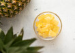 Dried soft sweet pineapple slices in glass bowl with raw pineapple on light table.Top view.