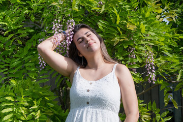 Wall Mural - woman in a blooming wisteria garden, around flowers. The girl holds a branch of lilac flowers in her hand