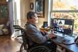 A man in a wheelchair at home, actively participating in a video call on his computer