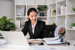 Focused Asian female accountant doing paperwork in office with plan documents on desk