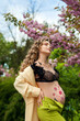 curly young girl pregnant near trees cherry blossoms, belly with flower, dreamy, in a sense of peace