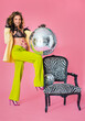 pregnant woman with disco ball standing by the chair. Belly with flower pattern, in bright pin-up clothes and underwear, fashionable studio photo on pink background