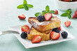 French toast crowned with vibrant strawberries, plump blackberries, and a fresh mint leaf, dusted delicately with powdered sugar. Served on a chic square plate.