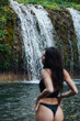 Women in bikini stand in front of a waterfall in Bali