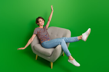 Wall Mural - Full size portrait of overjoyed gorgeous girl sit comfy chair raise hands rejoice isolated on green color background