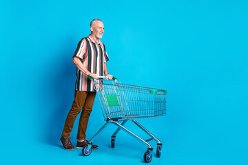 Sticker - Photo of handsome senior man wear summer stylish clothes hold pushcart empty space isolated on blue color background