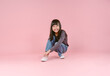 Cute little Asian girl sitting on the floor putting her shoes isolated in pink background