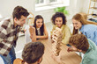 Top view photo of a happy young friends guys and girls playing together with wooden building blocks at home sitting at the table enjoying time together. Home leisure and board games concept.