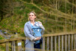 Happy woman looking to side while holding and carrying it in a baby carrier standing on a bridge