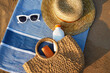 © artiemedvedev - Sunbathing accessories on sandy beach, straw hat beside sunglasses, sunblock lotion in bag for skin protection, summer seaside holiday essentials on striped towel, outdoor UV care on sunny day.
